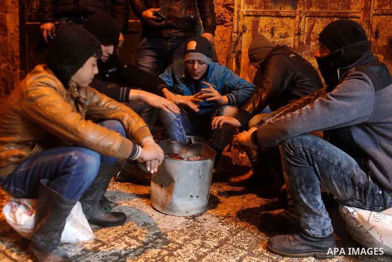 Palestinians warm themselves around a fire during a heavy winter storm in the West Bank city of Hebron, on January 26, 2016. Photo by Wisam Hashlamoun