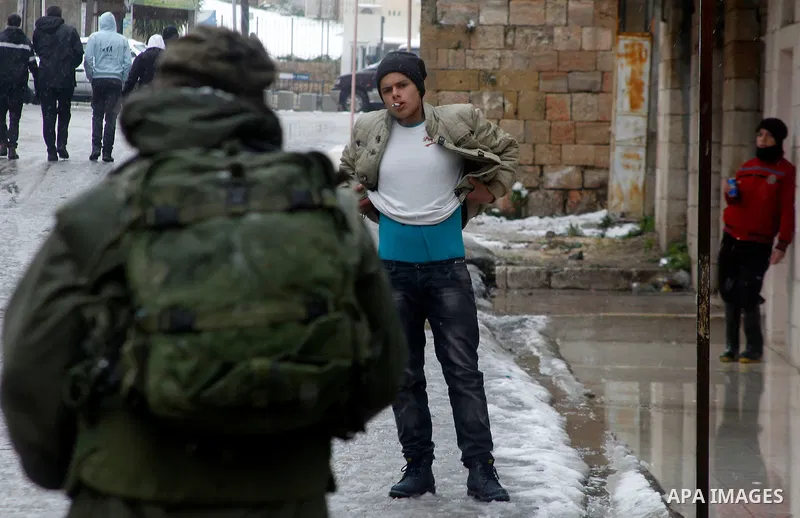 Israeli soldiers forces check Palestinians as they cross the street during a snowstorm in the West Bank city of Hebron, on January 26, 2016. Photo by Wisam Hashlamoun