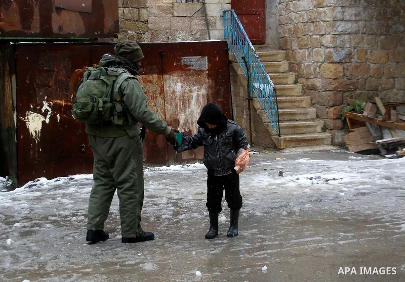 Israeli soldiers forces check Palestinians as they cross the street during a snowstorm in the West Bank city of Hebron, on January 26, 2016. Photo by Wisam Hashlamoun