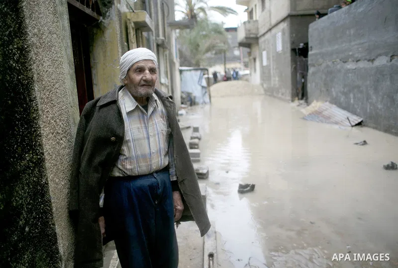 A Palestinian man stands on his doorstep looking at a flooded street following heavy rainfall in the southern Gaza Strip town of Rafah on January 26, 2016. Photo by Abed Rahim Khatib