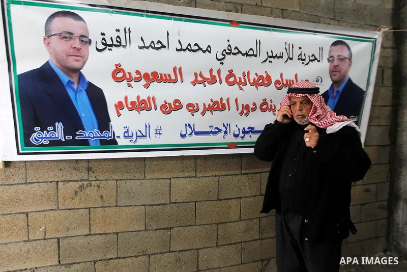 The father of Palestinian journalist Mohammed al-Qiq who is on hunger strike in an Israeli jail for 64 days stands past the banners of his son in front of a protest tent in the West Bank village of Dura on January 27, 20...