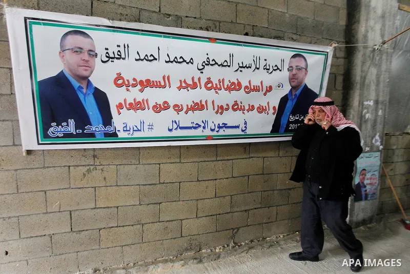 The father of Palestinian journalist Mohammed al-Qiq who is on hunger strike in an Israeli jail for 64 days stands past the banners of his son in front of a protest tent in the West Bank village of Dura on January 27, 20...