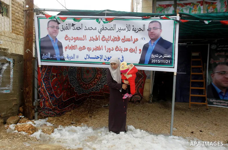 Fayha Shalash, the wife of Palestinian journalist Mohammed al-Qiq who is on hunger strike in an Israeli jail for 64 days holds her daughter in front of a protest tent in the West Bank village of Dura on January 27, 2016....
