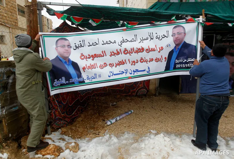 Palestinians hold the banners of Palestinian journalist Mohammed al-Qiq who is on hunger strike in an Israeli jail for 64 days in front of a protest tent in the West Bank village of Dura on January 27, 2016. Qiq went on...