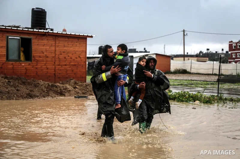 A picture taken on January 25, 2016 shows Members of Palestinian Civil Defence evacuation children, whose families house was destroyed during the 2014 war, after rain waters flooded their families shelter, in Khan Younis...