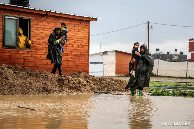 A picture taken on January 25, 2016 shows Members of Palestinian Civil Defence evacuation children, whose families house was destroyed during the 2014 war, after rain waters flooded their families shelter, in Khan Younis...