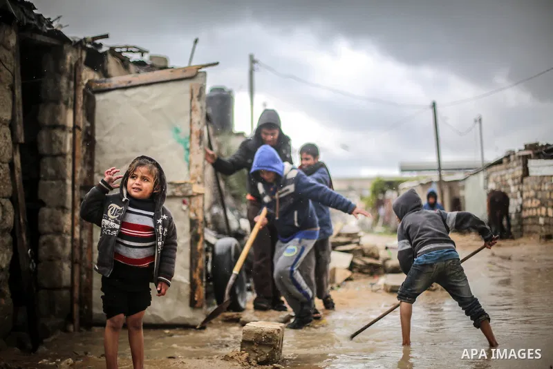 A picture taken on January 25, 2016 shows Palestinians children remove rainwater outside their families house following heavy rainfall, in Khan Younis in the southern Gaza Strip. Photo by Mohammed Dahman