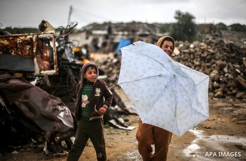 A picture taken on January 25, 2016 shows Palestinian children cross a flooded road on a rainy day, in Khan Younis in the southern Gaza Strip. Photo by Mohammed Dahman