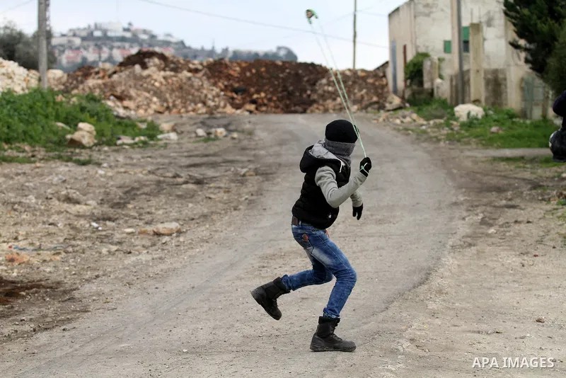 A Palestinian protester uses a slingshot to hurl stones toward Israeli security forces during clashes following a protest against the expropriation of Palestinian land by Israel in the West Bank village of Kafr Qaddum, n...