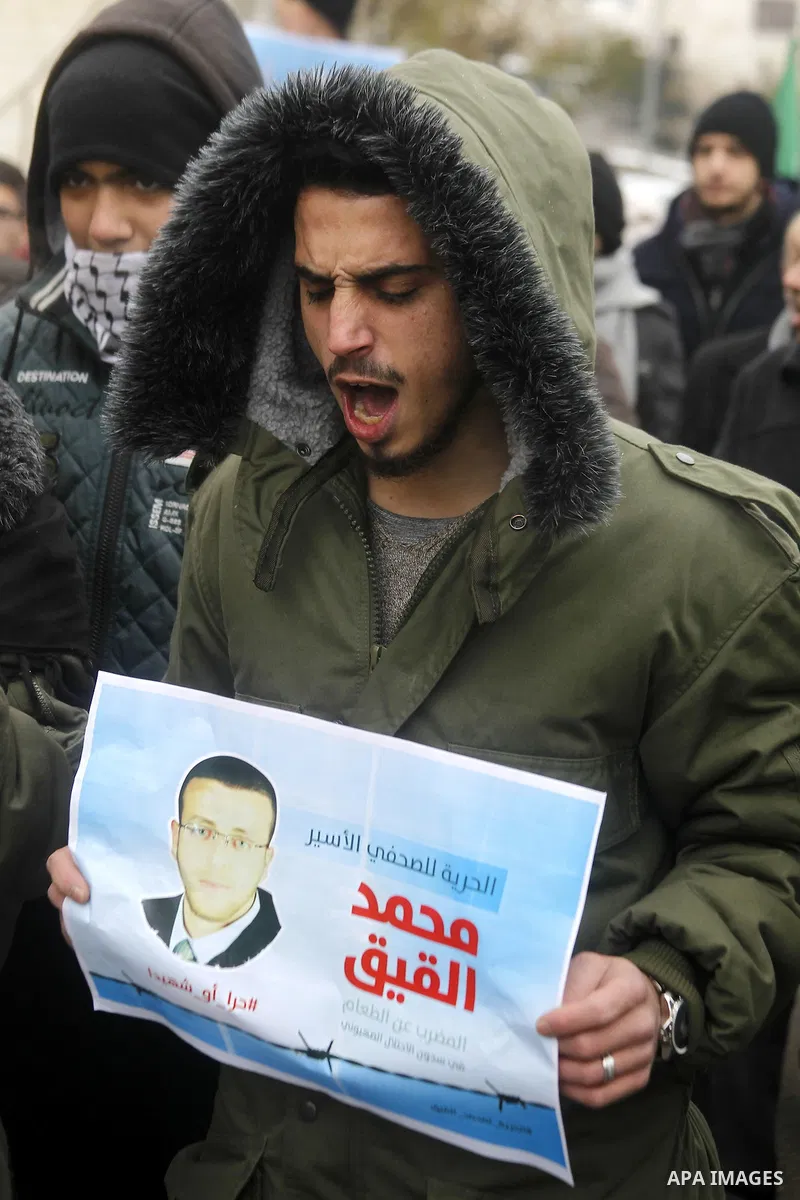 A Palestinian man holds a poster bearing a portrait of Palestinian journalist Mohammed al-Qiq who is imprisoned in an Israeli jail during a protest in support of his hunger strike in the West Bank city of Hebron on Janua...