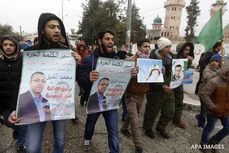Palestinians hold posters bearing a portrait of Palestinian journalist Mohammed al-Qiq who is imprisoned in an Israeli jail during a protest in support of his hunger strike in the West Bank city of Hebron on January 29,...