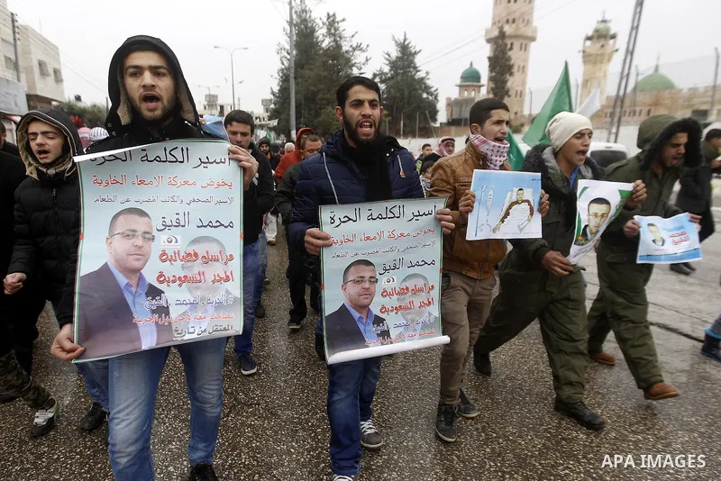 Palestinians hold posters bearing a portrait of Palestinian journalist Mohammed al-Qiq who is imprisoned in an Israeli jail during a protest in support of his hunger strike in the West Bank city of Hebron on January 29,...