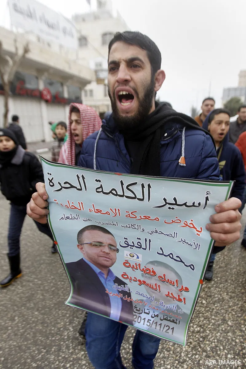 A Palestinian man holds a poster bearing a portrait of Palestinian journalist Mohammed al-Qiq who is imprisoned in an Israeli jail during a protest in support of his hunger strike in the West Bank city of Hebron on Janua...