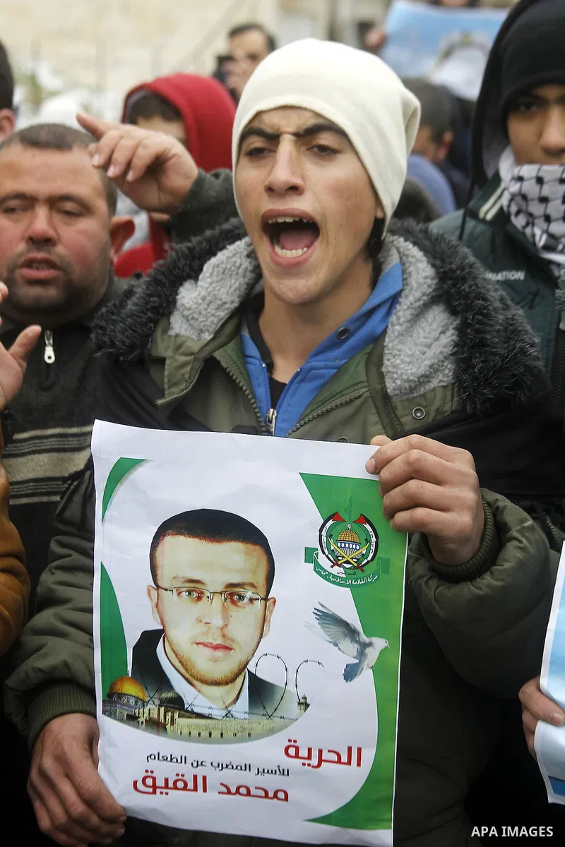 A Palestinian man holds a poster bearing a portrait of Palestinian journalist Mohammed al-Qiq who is imprisoned in an Israeli jail during a protest in support of his hunger strike in the West Bank city of Hebron on Janua...