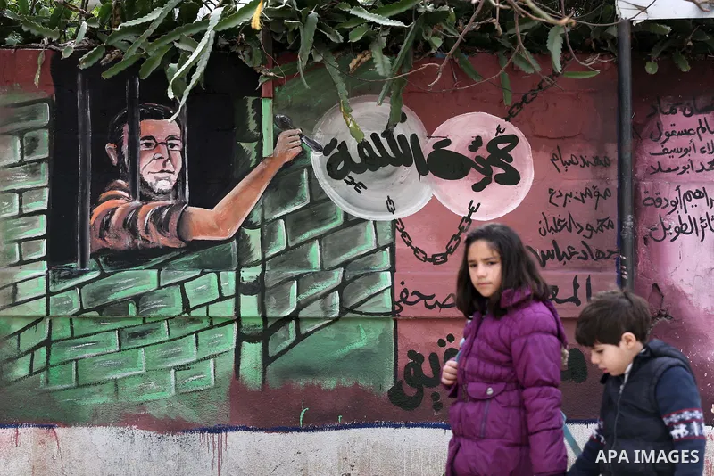 Palestinians walk past a mural depicts journalist Mohammed al-Qiq who is imprisoned in an Israeli jail at the Ministry of Prisoners, in Gaza City, on January 30, 2016. Qiq is being held under Israel's controversial admin...