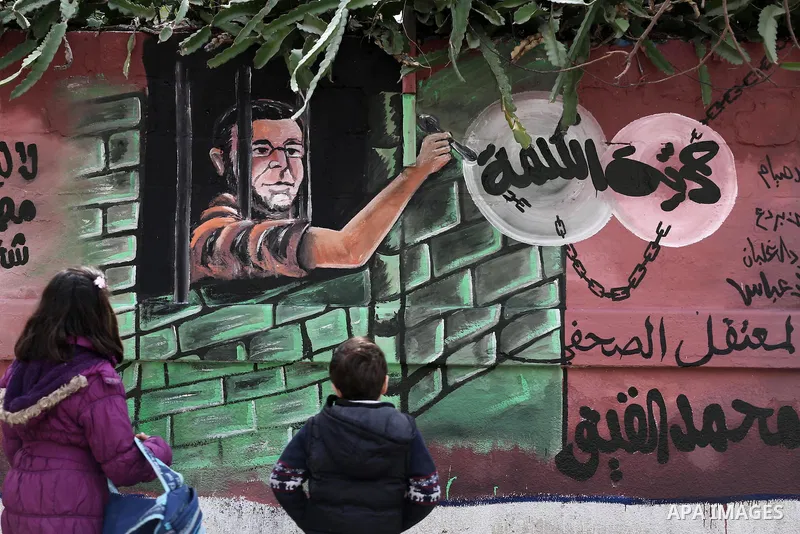 Palestinians walk past a mural depicts journalist Mohammed al-Qiq who is imprisoned in an Israeli jail at the Ministry of Prisoners, in Gaza City, on January 30, 2016. Qiq is being held under Israel's controversial admin...