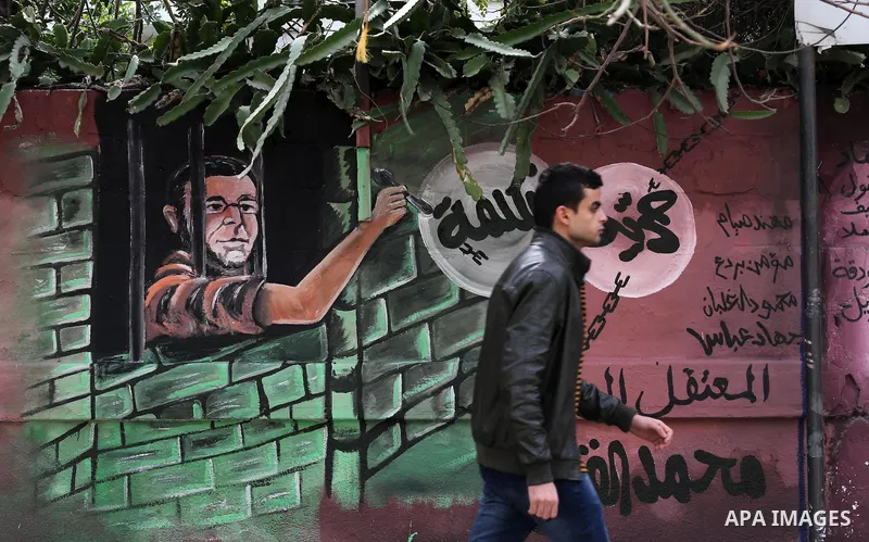 Palestinians walk past a mural depicts journalist Mohammed al-Qiq who is imprisoned in an Israeli jail at the Ministry of Prisoners, in Gaza City, on January 30, 2016. Qiq is being held under Israel's controversial admin...