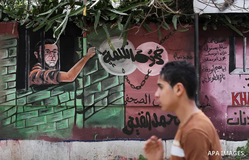 Palestinians walk past a mural depicts journalist Mohammed al-Qiq who is imprisoned in an Israeli jail at the Ministry of Prisoners, in Gaza City, on January 30, 2016. Qiq is being held under Israel's controversial admin...