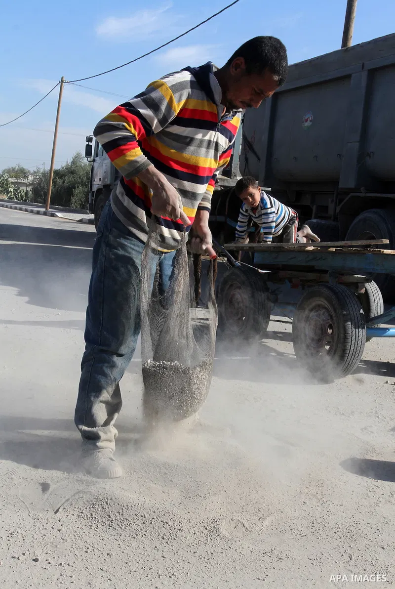 A Palestinian man collects the gravel which falling from trucks loaded with cement after it entered through the Kerem Shalom crossing in Rafah, to sell to customers, on January 31, 2016. Photo by Abed Rahim Khatib