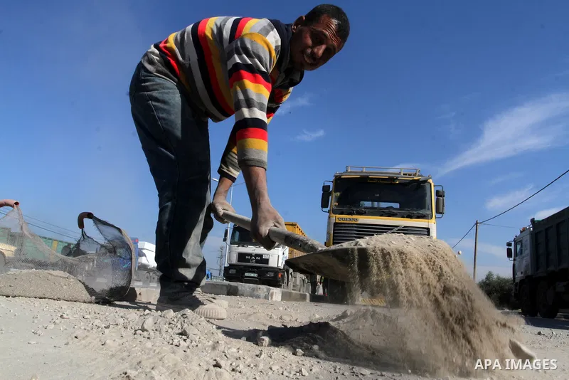 A Palestinian man collects the gravel which falling from trucks loaded with cement after it entered through the Kerem Shalom crossing in Rafah, to sell to customers, on January 31, 2016. Photo by Abed Rahim Khatib