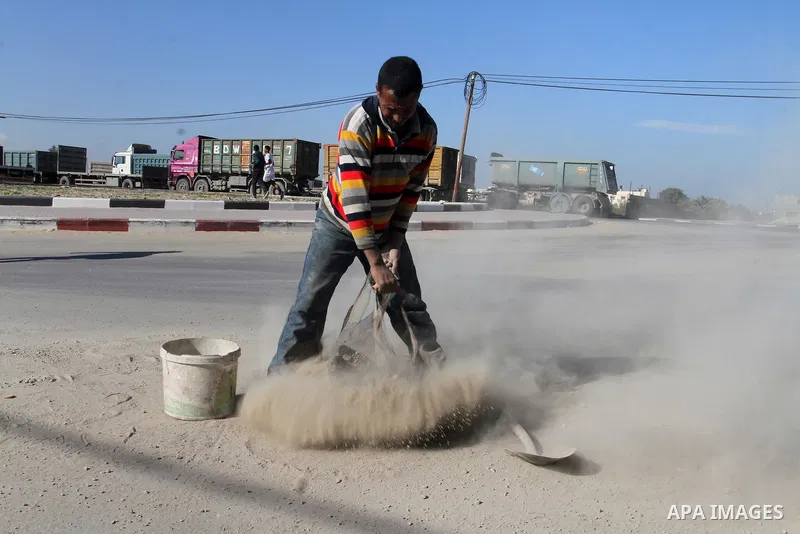 A Palestinian man collects the gravel which falling from trucks loaded with cement after it entered through the Kerem Shalom crossing in Rafah, to sell to customers, on January 31, 2016. Photo by Abed Rahim Khatib