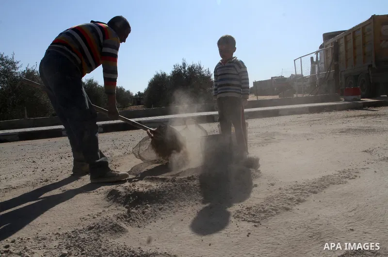 A Palestinian man collects the gravel which falling from trucks loaded with cement after it entered through the Kerem Shalom crossing in Rafah, to sell to customers, on January 31, 2016. Photo by Abed Rahim Khatib