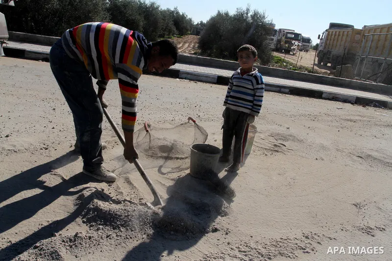 A Palestinian man collects the gravel which falling from trucks loaded with cement after it entered through the Kerem Shalom crossing in Rafah, to sell to customers, on January 31, 2016. Photo by Abed Rahim Khatib