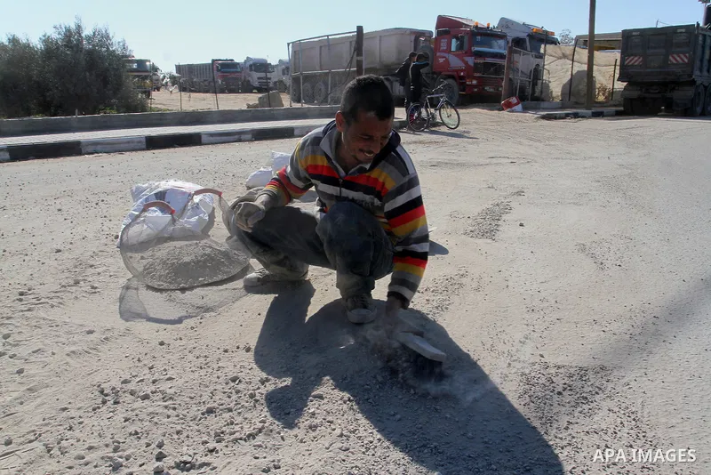 A Palestinian man collects the gravel which falling from trucks loaded with cement after it entered through the Kerem Shalom crossing in Rafah, to sell to customers, on January 31, 2016. Photo by Abed Rahim Khatib