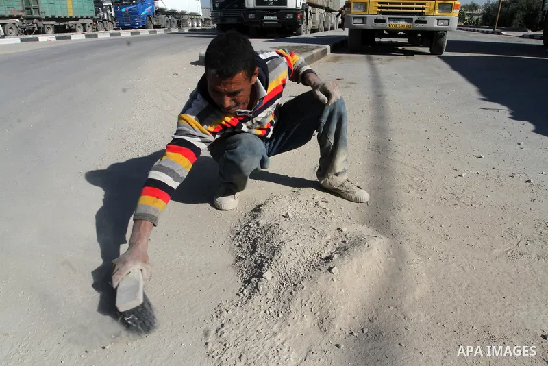 A Palestinian man collects the gravel which falling from trucks loaded with cement after it entered through the Kerem Shalom crossing in Rafah, to sell to customers, on January 31, 2016. Photo by Abed Rahim Khatib