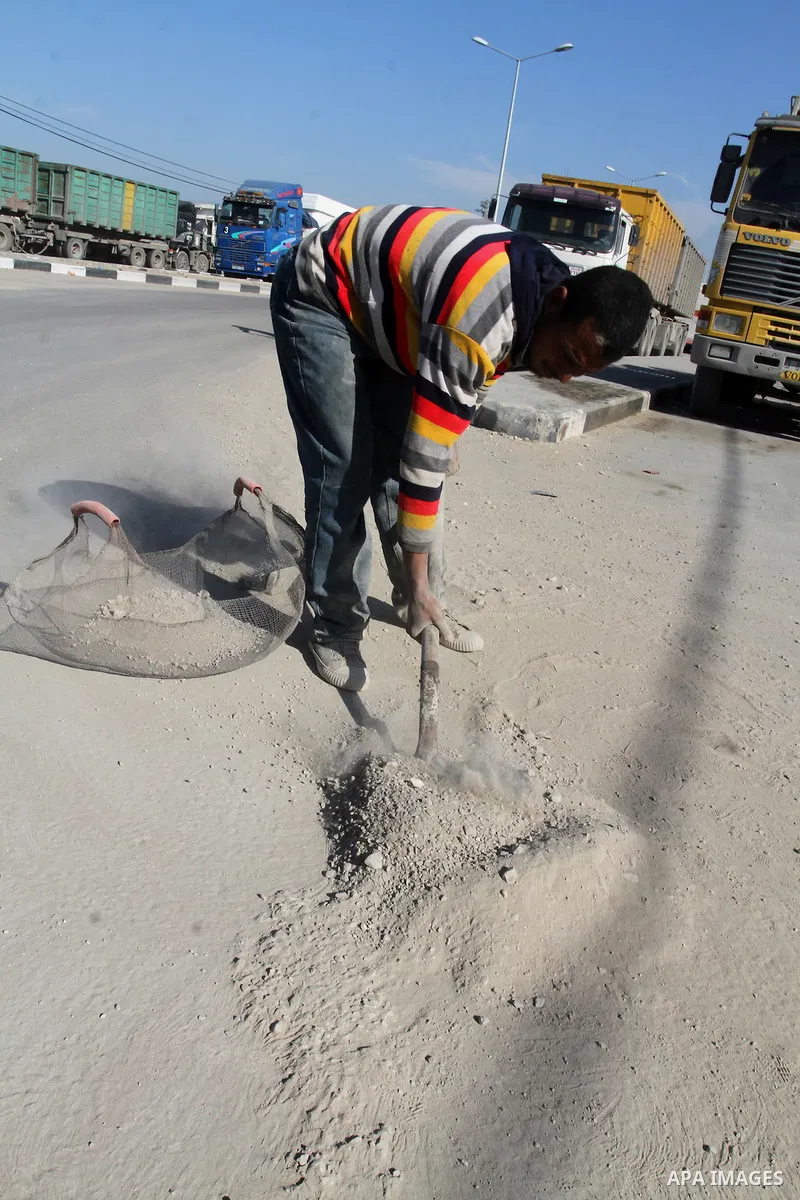 A Palestinian man collects the gravel which falling from trucks loaded with cement after it entered through the Kerem Shalom crossing in Rafah, to sell to customers, on January 31, 2016. Photo by Abed Rahim Khatib