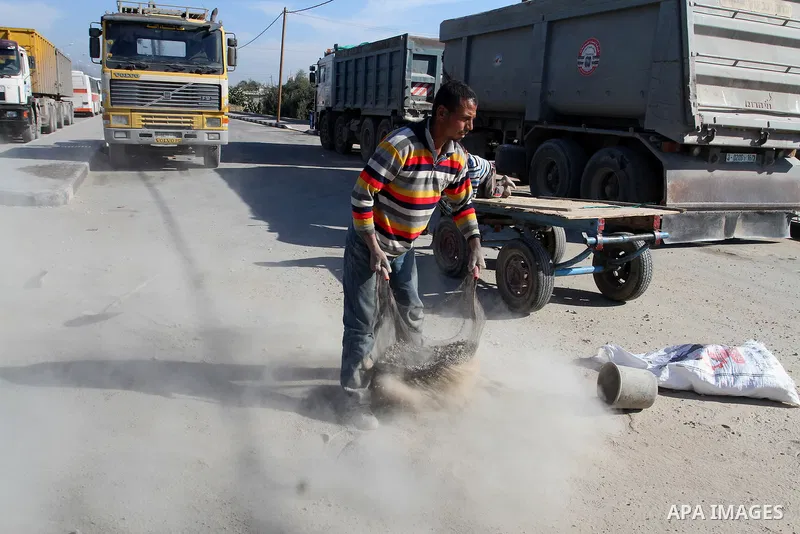 A Palestinian man collects the gravel which falling from trucks loaded with cement after it entered through the Kerem Shalom crossing in Rafah, to sell to customers, on January 31, 2016. Photo by Abed Rahim Khatib