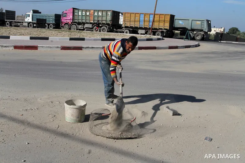 A Palestinian man collects the gravel which falling from trucks loaded with cement after it entered through the Kerem Shalom crossing in Rafah, to sell to customers, on January 31, 2016. Photo by Abed Rahim Khatib
