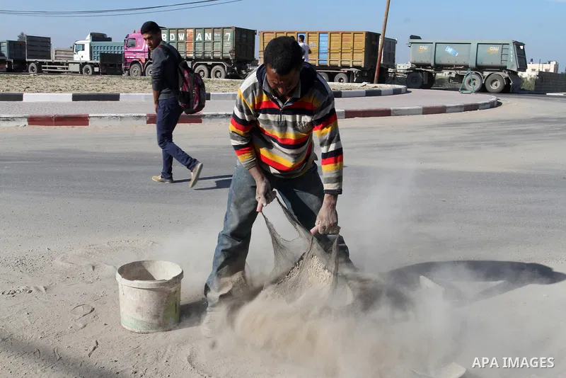 A Palestinian man collects the gravel which falling from trucks loaded with cement after it entered through the Kerem Shalom crossing in Rafah, to sell to customers, on January 31, 2016. Photo by Abed Rahim Khatib