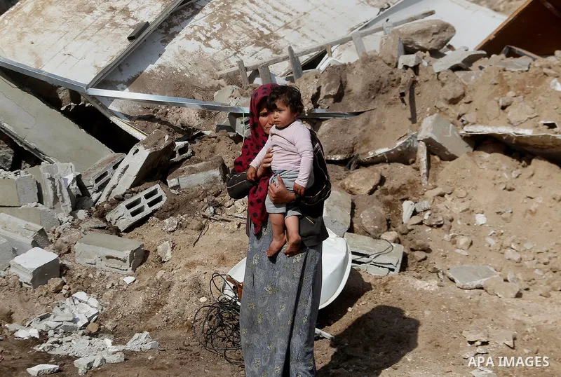 A Palestinian woman stands holding a child next to items salvaged from the remains of their home after it was demolished by Israeli bulldozers in a disputed military zone in the area of Musafir Jenbah, which includes sev...