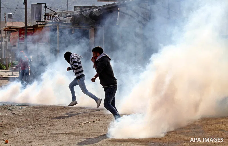 Palestinian protesters take cover from a tear gas canister fired by Israeli security forces during clashes in the Palestinian town of Qabatiya, near Jenin in the north of the Israeli-occupied West Bank, on February 5, 20...