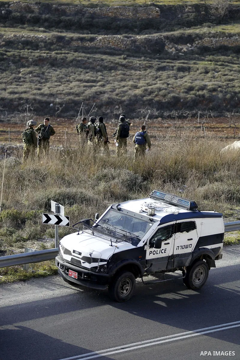 Israeli security forces monitor the area as their colleagues give back the body of Haitham al-Bau, who was shot dead by Israeli soldiers after throwing a petrol bomb at a military jeep, to members of the Palestinian Red...