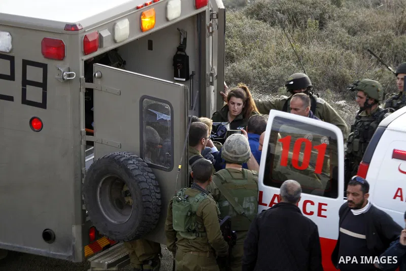 Israeli security forces in a military ambulance stand next to a stretcher carrying the body of Haitham al-Bau, who was shot dead by Israeli soldiers after throwing a petrol bomb at a military jeep, as they hand over the...