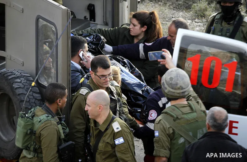 Israeli security forces in a military ambulance stand next to a stretcher carrying the body of Haitham al-Bau, who was shot dead by Israeli soldiers after throwing a petrol bomb at a military jeep, as they hand over the...