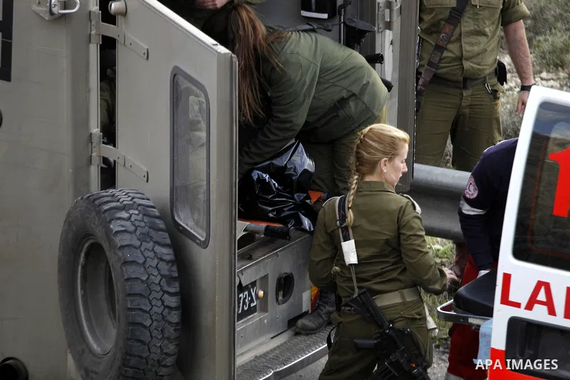 Israeli security forces in a military ambulance stand next to a stretcher carrying the body of Haitham al-Bau, who was shot dead by Israeli soldiers after throwing a petrol bomb at a military jeep, as they hand over the...