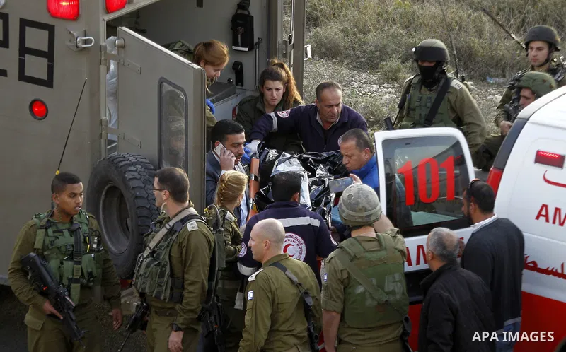 Israeli security forces in a military ambulance stand next to a stretcher carrying the body of Haitham al-Bau, who was shot dead by Israeli soldiers after throwing a petrol bomb at a military jeep, as they hand over the...