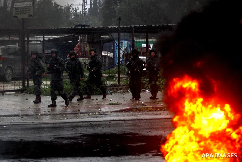 Israeli soldiers walk near a burning tyre during clashes with Palestinians in the West Bank town of Qabatya, near Jenin February 6, 2016. On Wednesday, three young Palestinian men from Qabatya wielding guns, knives and p...