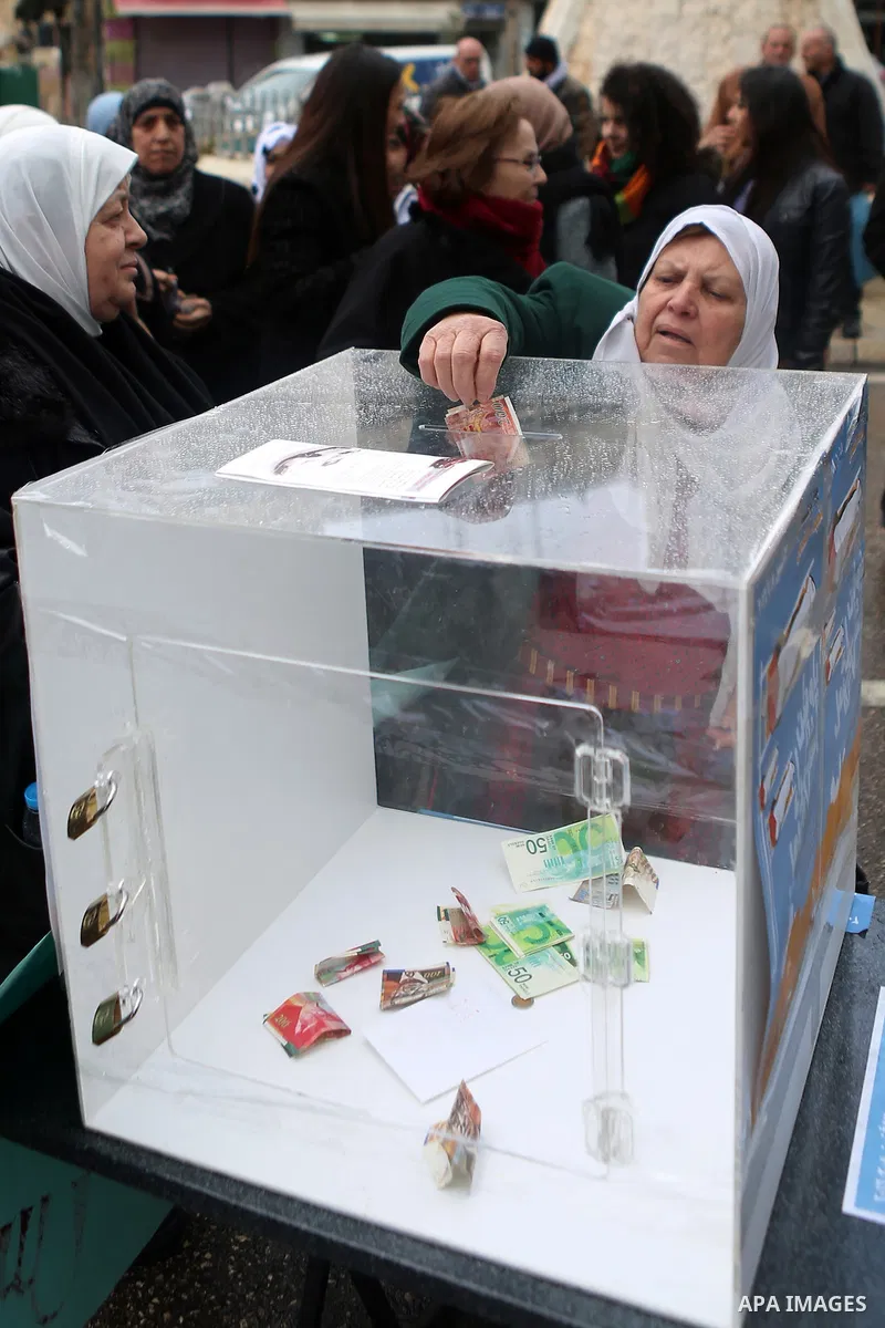 A Palestinian woman donates money during a fundraising campaign aimed at rebuilding the families houses of Jerusalem Martyrs, after demolished by Israeli authorities in the West Bank city of Ramallah, on February 8, 2016...
