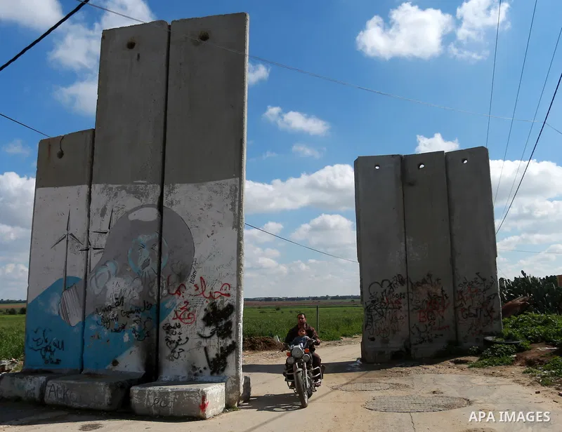 A Palestinian man rides amotocecly while An Israeli drill works near the Israeli side of border with the southern Gaza Strip trying to discover tunnels on February 11, 2016. Photo by Yasser Qudih