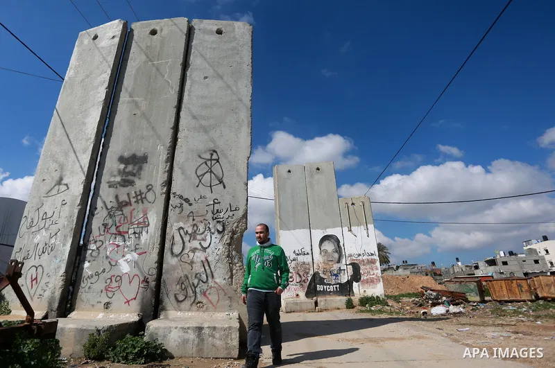 A Palestinian man walks at street while An Israeli drill works near the Israeli side of border with the southern Gaza Strip trying to discover tunnels on February 11, 2016. Photo by Yasser Qudih
