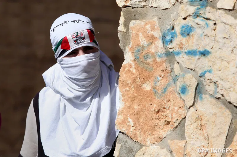 A masked Palestinian protester takes cover during clashes with Israeli security forces following a protest against the expropriation of Palestinian land by Israel in the West Bank village of Kafr Qaddum, near the norther...