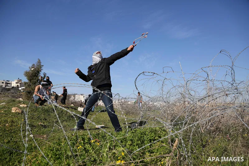 A Palestinian protester uses a slingshot to hurls stones toward israeli security forces during clashes following a demonstration in solidarity with Palestinian prisoners in Israeli jails, outside the compound of the Isra...