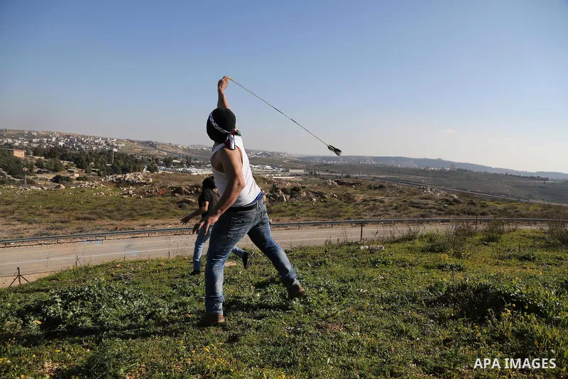 A Palestinian protester uses a slingshot to hurls stones toward israeli security forces during clashes following a demonstration in solidarity with Palestinian prisoners in Israeli jails, outside the compound of the Isra...