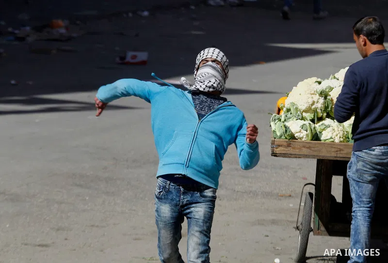 A Palestinian protester hurls stones toward Israeli security forces during clashes following the funeral of Kalzar al-Uweiwi, a Palestinian teenager who was killed a day earlier following a reported stabbing attack, in t...