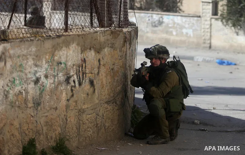 An Israeli soldier aims his weapon at Palestinian protesters during clashes in al-Amari refugee camp near the West Bank city of Ramallah February 15, 2016. Photo by Shadi Hatem