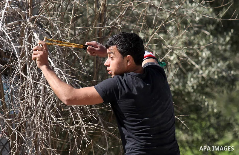 A Palestinian protester uses a slingshot to hurl stones toward Israeli security forces during clashes in the village of Araka, West of Jenin in the Israeli occupied West Bank on February 15, 2016. Photo by Nedal Eshtayah